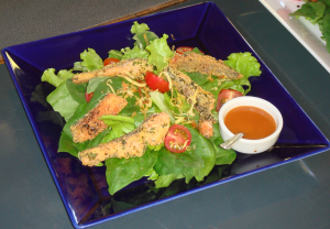Foto de um prato de peixe servido com alface, tomate e um molho avermelhado com um colher.